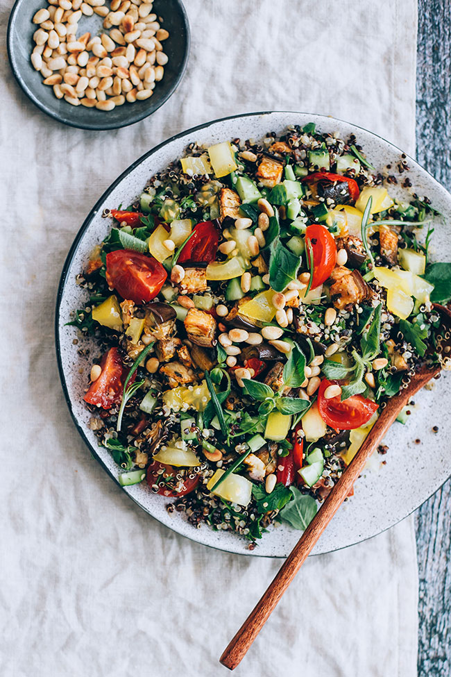 A big plate of Mediterranean quinoa salad with a small bowl of pine nuts off to the side.