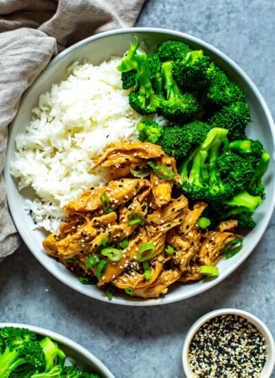 One bowl filled with white rice, chicken teriyaki and steamed broccoli garnished with sesame seeds and green onions.
