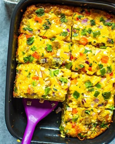 A cooked sausage hashbrown breakfast casserole in a black casserole dish cut into 8 pieces with a spatula picking up a piece.