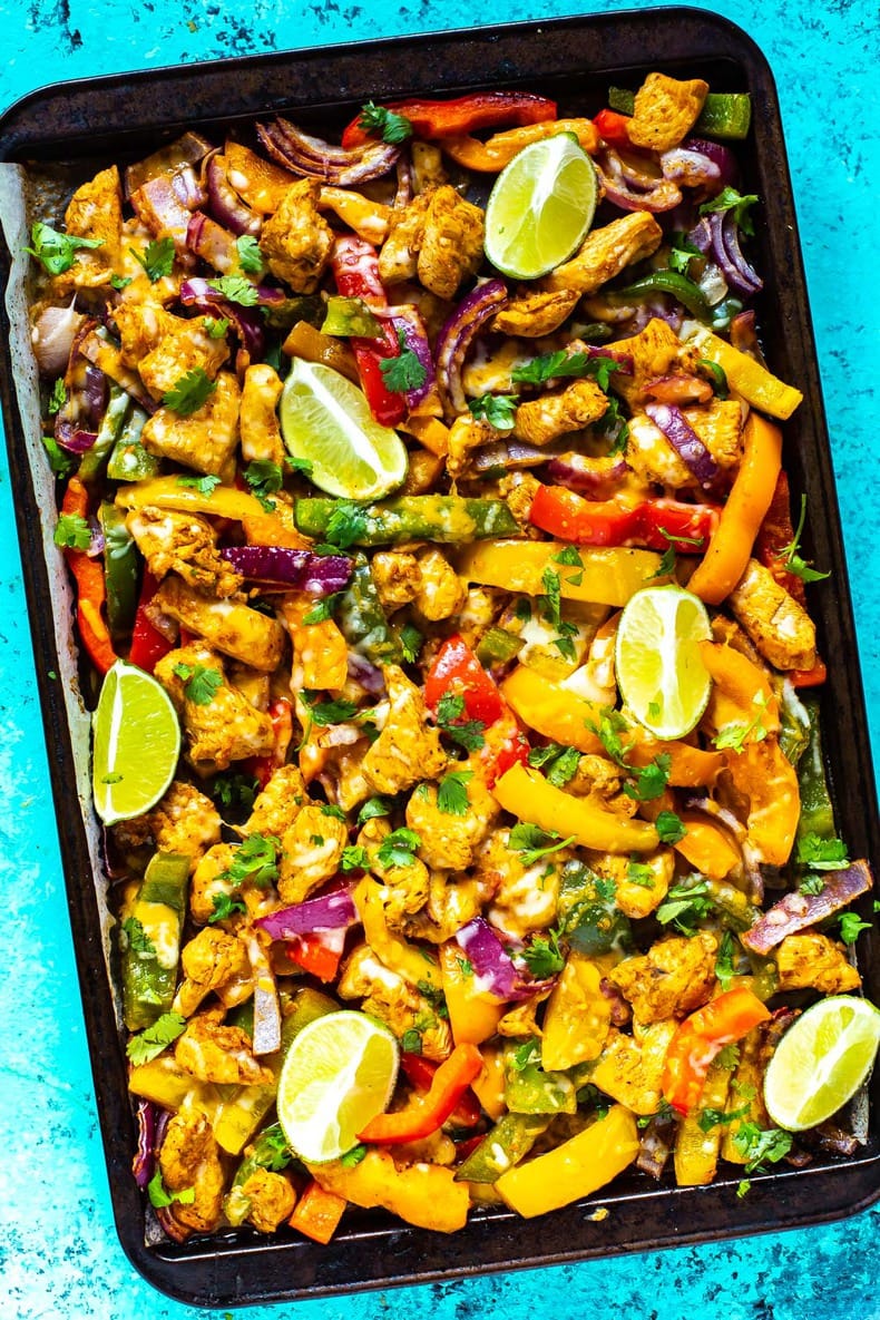 A sheet pan with chicken fajitas topped with lime slices and garnished with cilantro.
