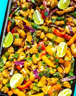 A close-up of a sheet pan with chicken fajitas topped with lime slices and garnished with cilantro.