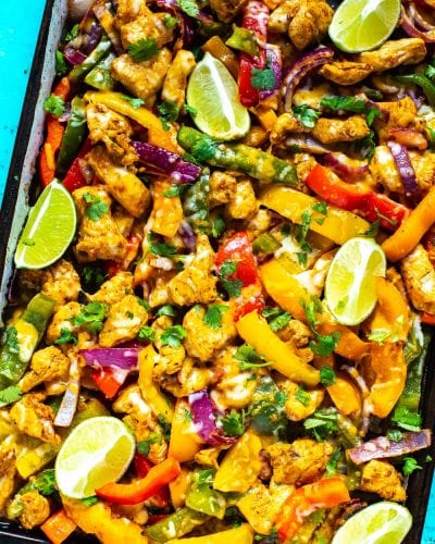 A close-up of a sheet pan with chicken fajitas topped with lime slices and garnished with cilantro.