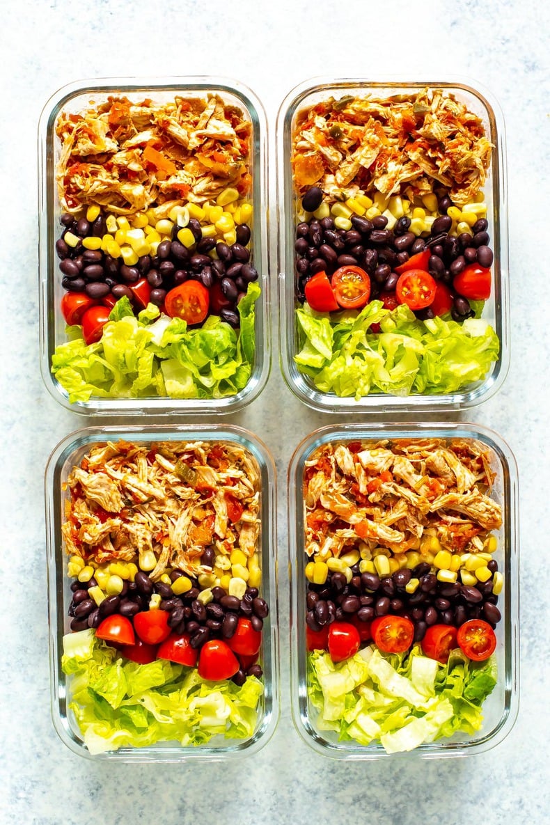Four meal prep containers, each containing crockpot salsa chicken, corn, black beans, cherry tomatoes and lettuce.