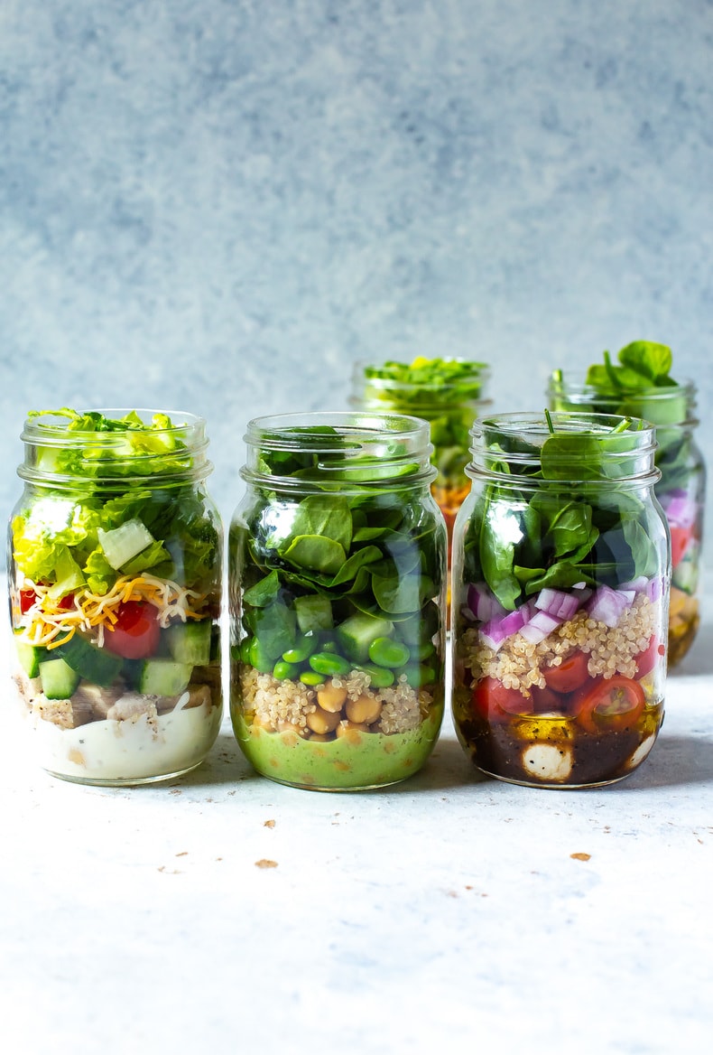 3 mason jars in a row, each containing a different salad inside.