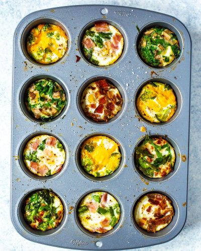 A muffin tin filled with 5 different types of baked eggs - mushroom spinach, sundried tomato & arugula, bacon, ham & asparagus, and broccoli cheddar.