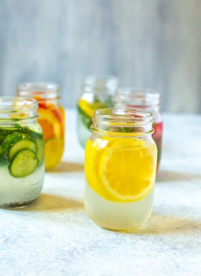 Lemon Water 5 Ways in mason jars. Focus on the lemon wedge water.