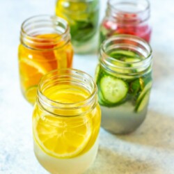 Lemon Water 5 Ways in mason jars with lemon wedge water in front.