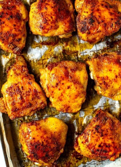 A close-up of seasoned baked chicken thighs on a sheet pan with prepared with parchment paper.