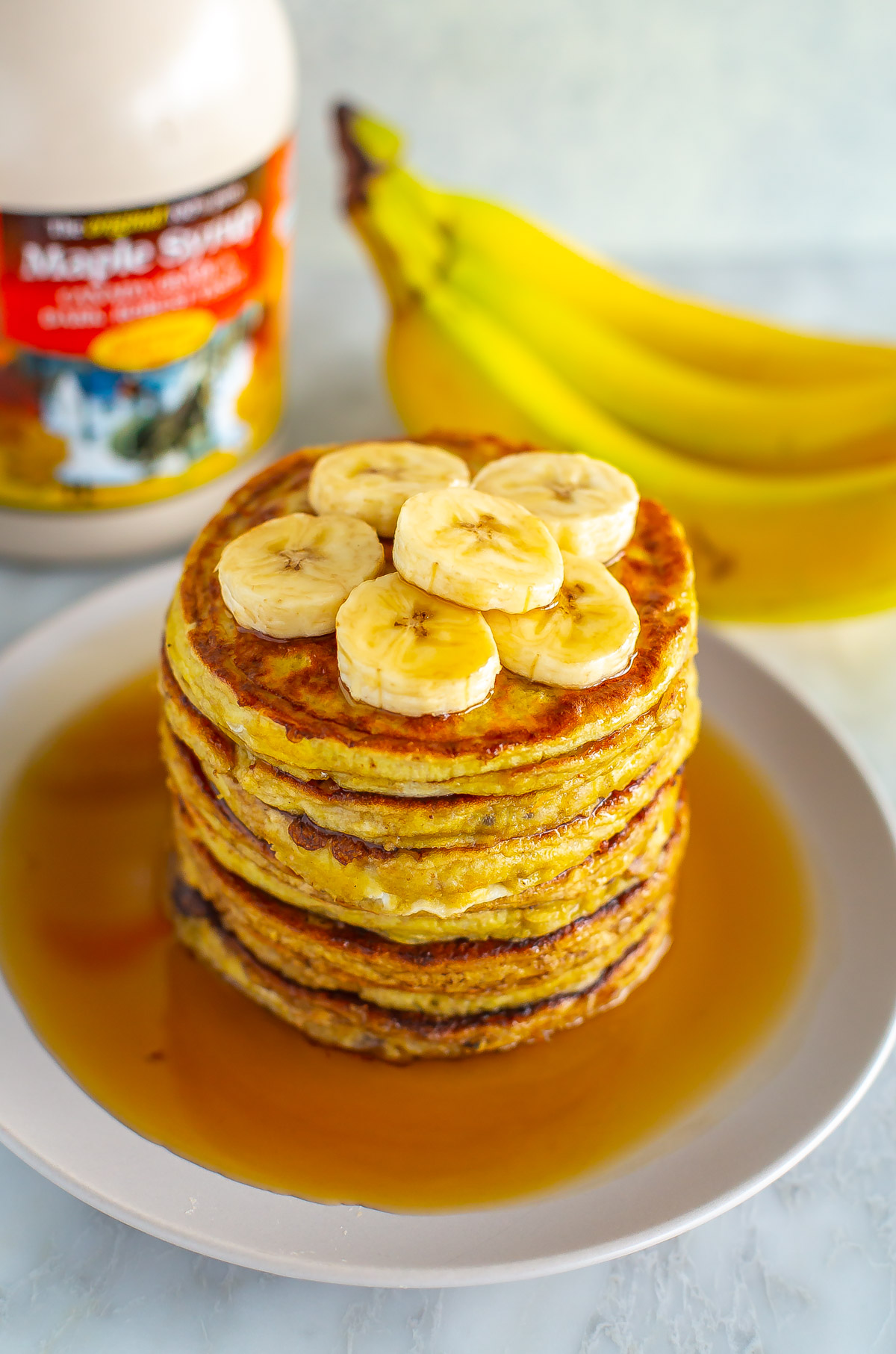 A close-up of banana egg pancakes with maple syrup drizzled over top.