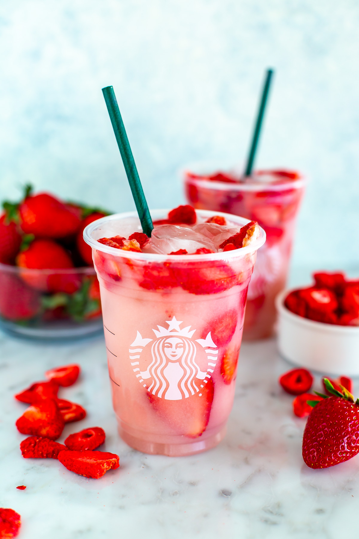 Two cups of homemade Starbucks pink drink with freeze-dried strawberries placed around them.