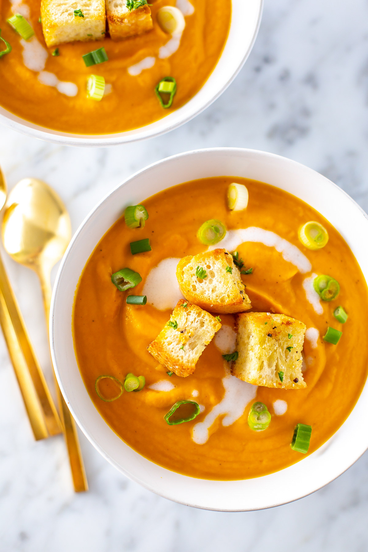 A close up of a bowl of creamy coconut carrot ginger soup topped with croutons. 