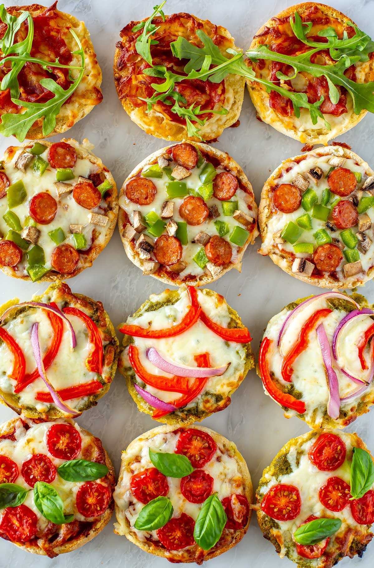 A close-up of 12 english muffin pizzas on a marble slab.