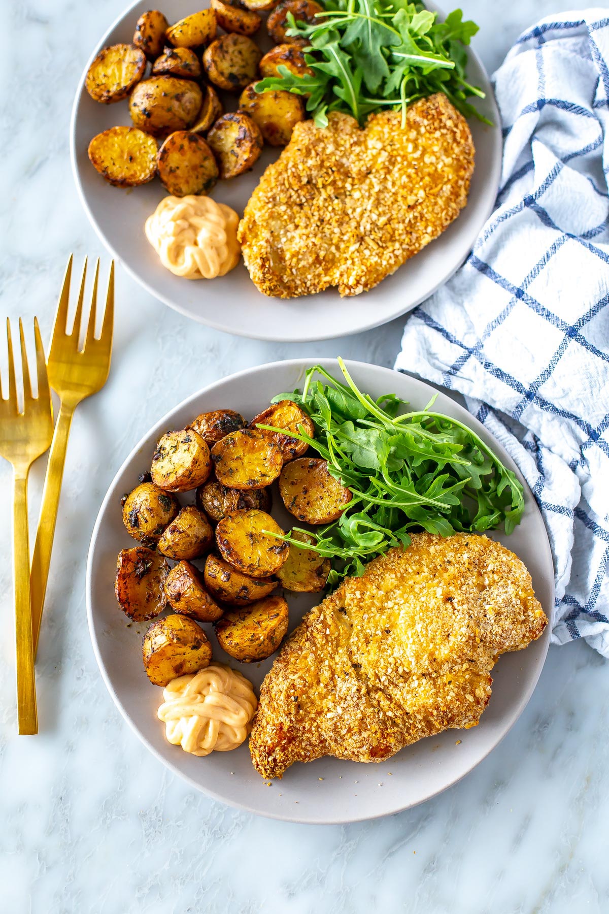 Two plates, each with a chicken cutlet, lemon dill potatoes and a side of arugula.