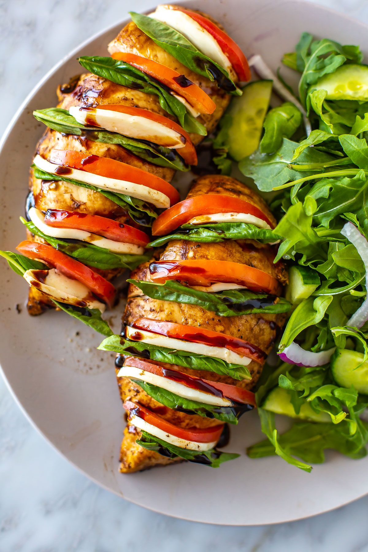 A close-up of a plate with hasselback caprese chicken with a side salad.