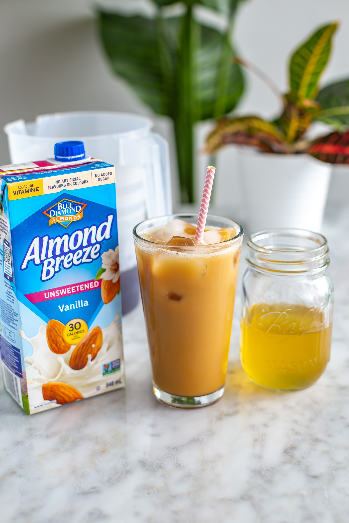 A glass of honey almond cold brew placed next to a carton of almond milk and honey almond syrup.