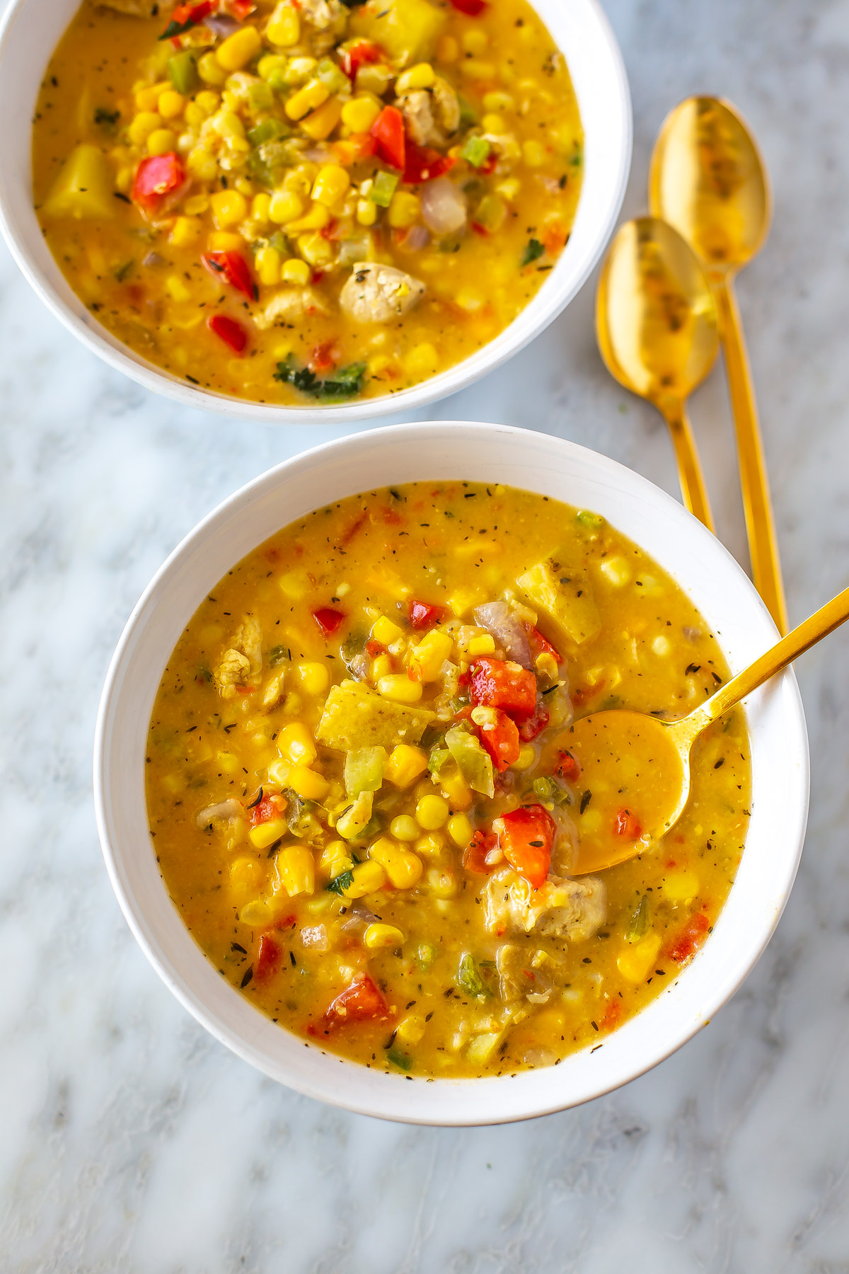 Two bowls of chicken corn chowder with a spoon in one of them.
