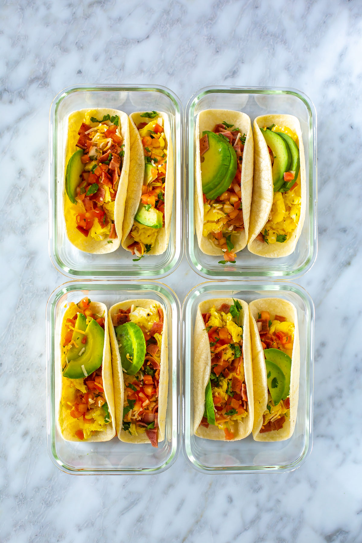 Four meal prep containers, each with two breakfast tacos inside.