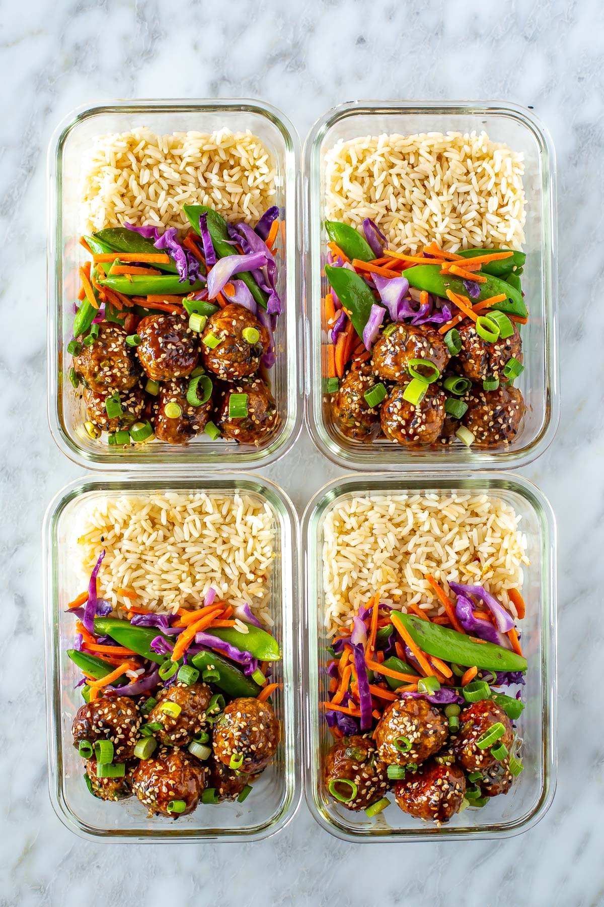 Four meal prep containers, each filled with rice, stir fried veggies and sticky teriyaki chicken meatballs.