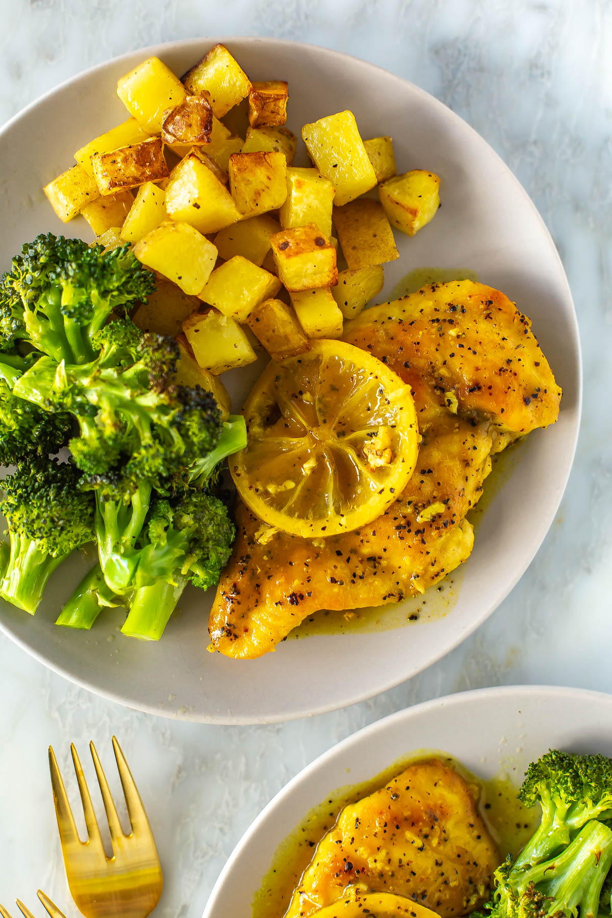 A close-up of a plate with lemon pepper chicken with a side of roasted potatoes and roasted broccoli.
