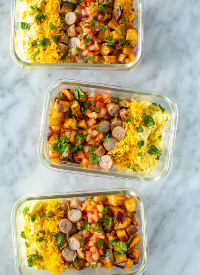 Three meal prep containers, each filled with roasted vegetables, scrambled eggs, and cooked sausage.
