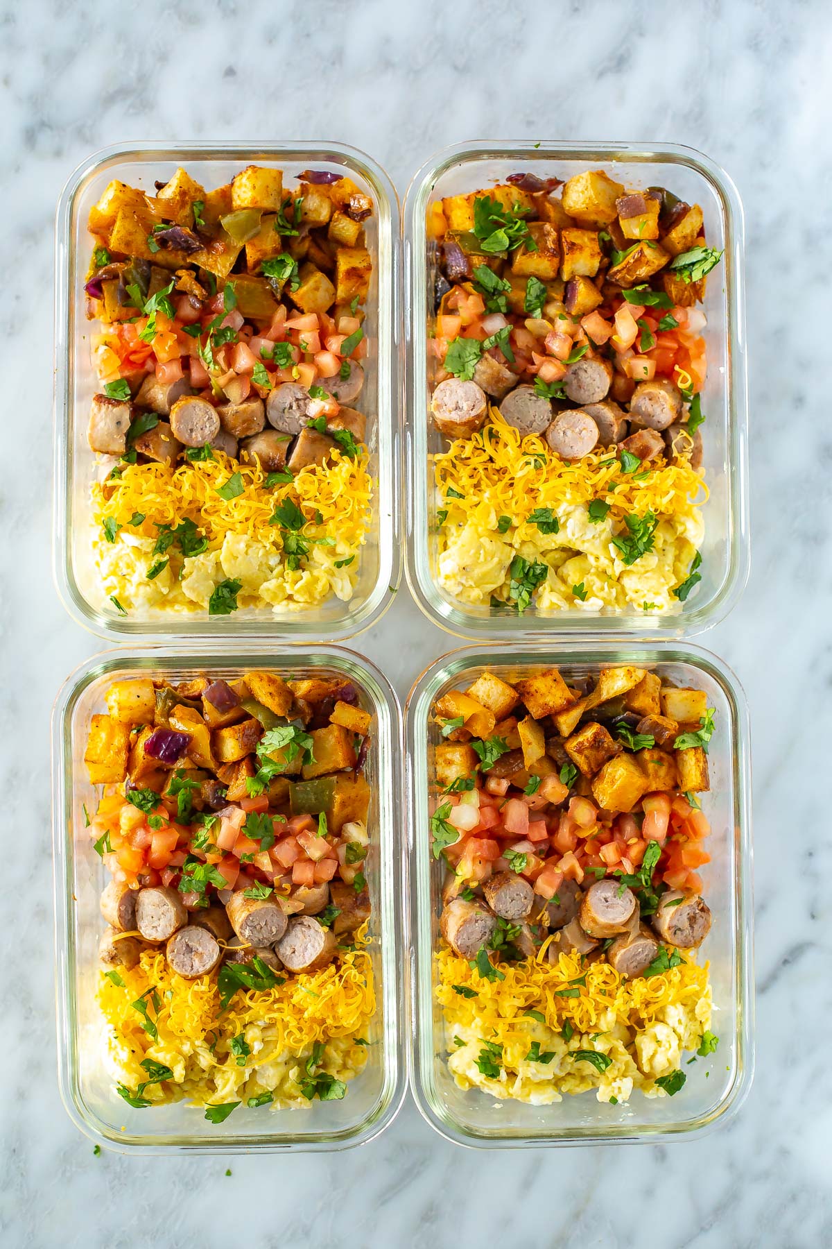 Four meal prep containers filled with roasted veggies, scrambled eggs, and cooked sausage.