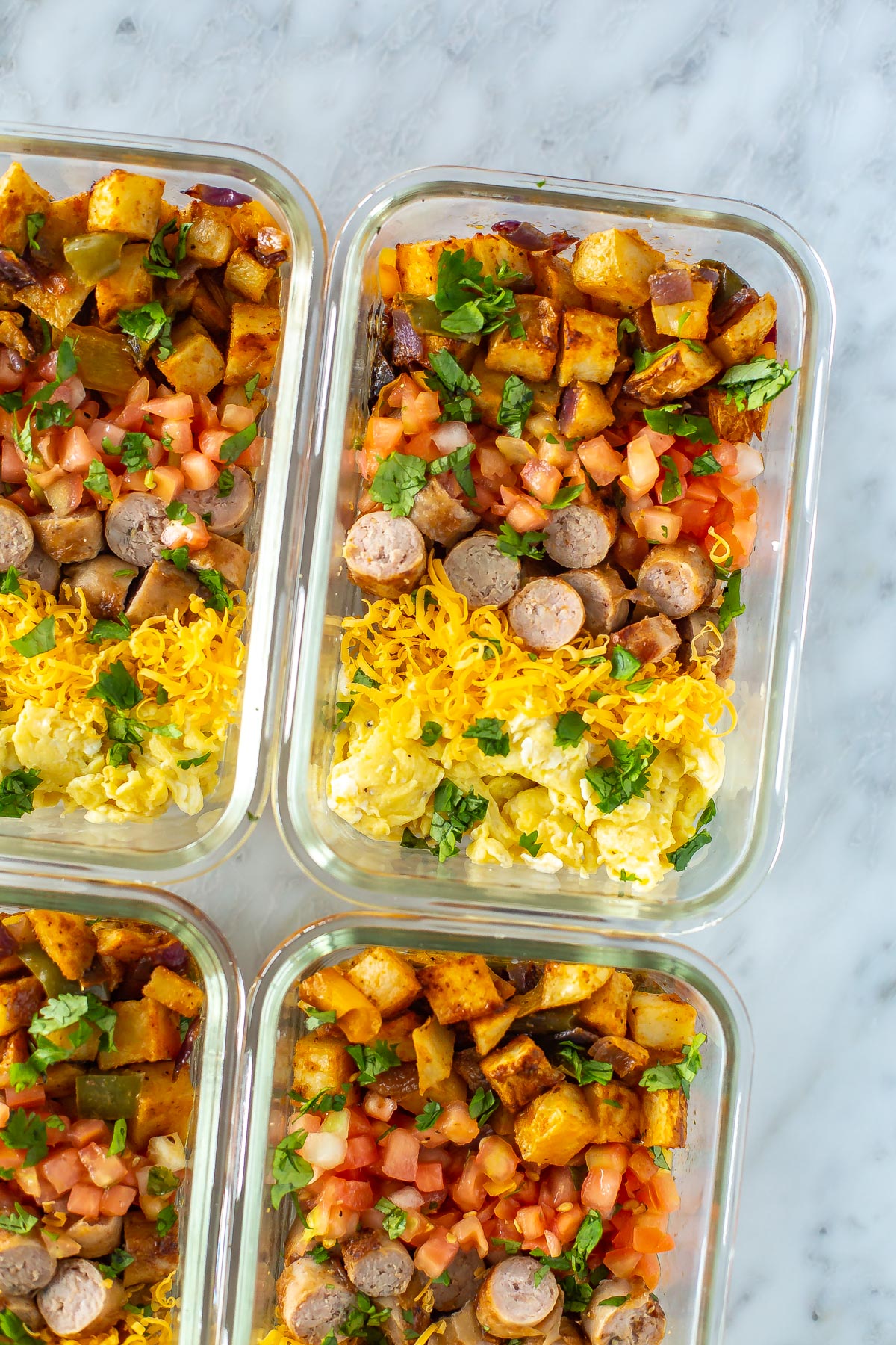 Four meal prep containers filled with roasted veggies, scrambled eggs, and cooked sausage.