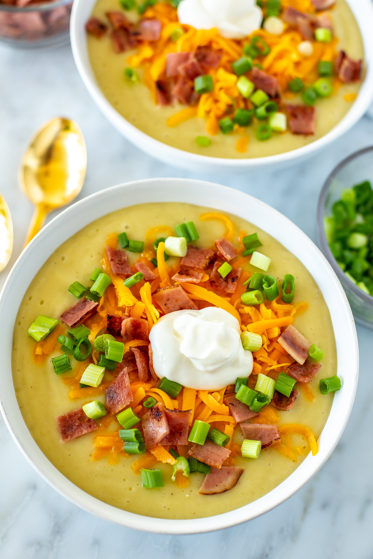 A close-up of a bowl of crockpot potato soup topped with green onions, cheese, bacon, and sour cream.