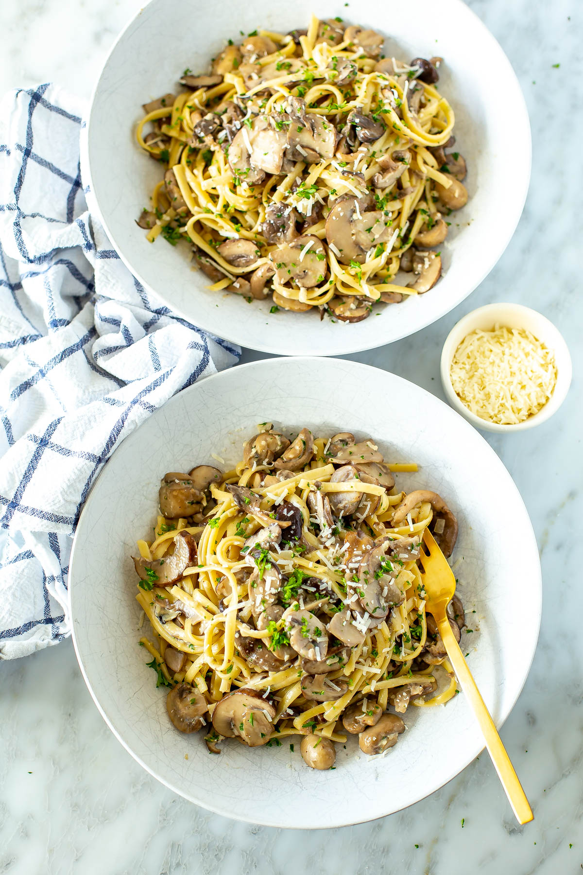 Two bowls of creamy mushroom pasta with a small bowl of parmesan cheese on the side.