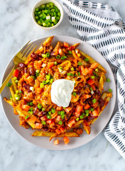 A big plate with chili cheese fries on top, loaded with tomato, green onions and sour cream.