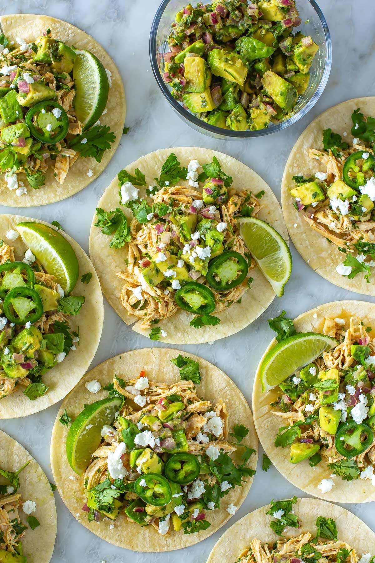 Multiple cilantro lime chicken tacos topped with avocado salsa and feta cheese.
