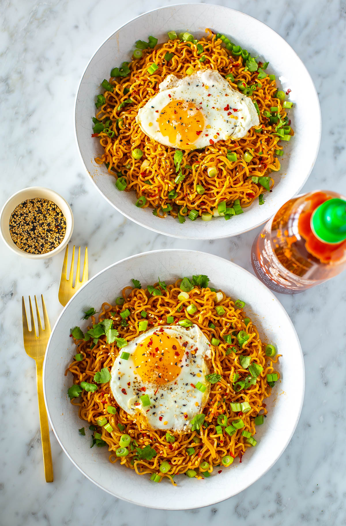 Two bowls of spicy noodles, each topped with a fried egg and green onions.