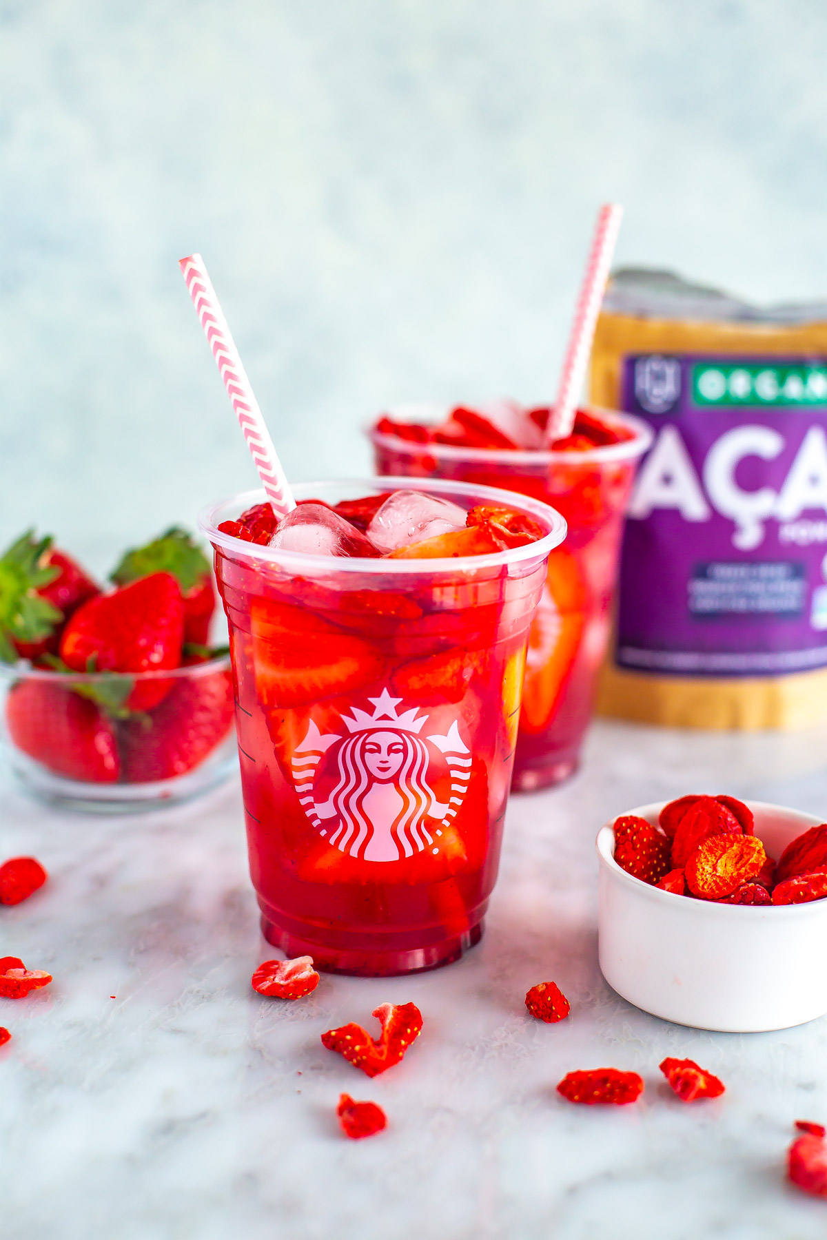 Two glasses of copycat Starbucks strawberry acai refreshers with ingredients placed behind them.