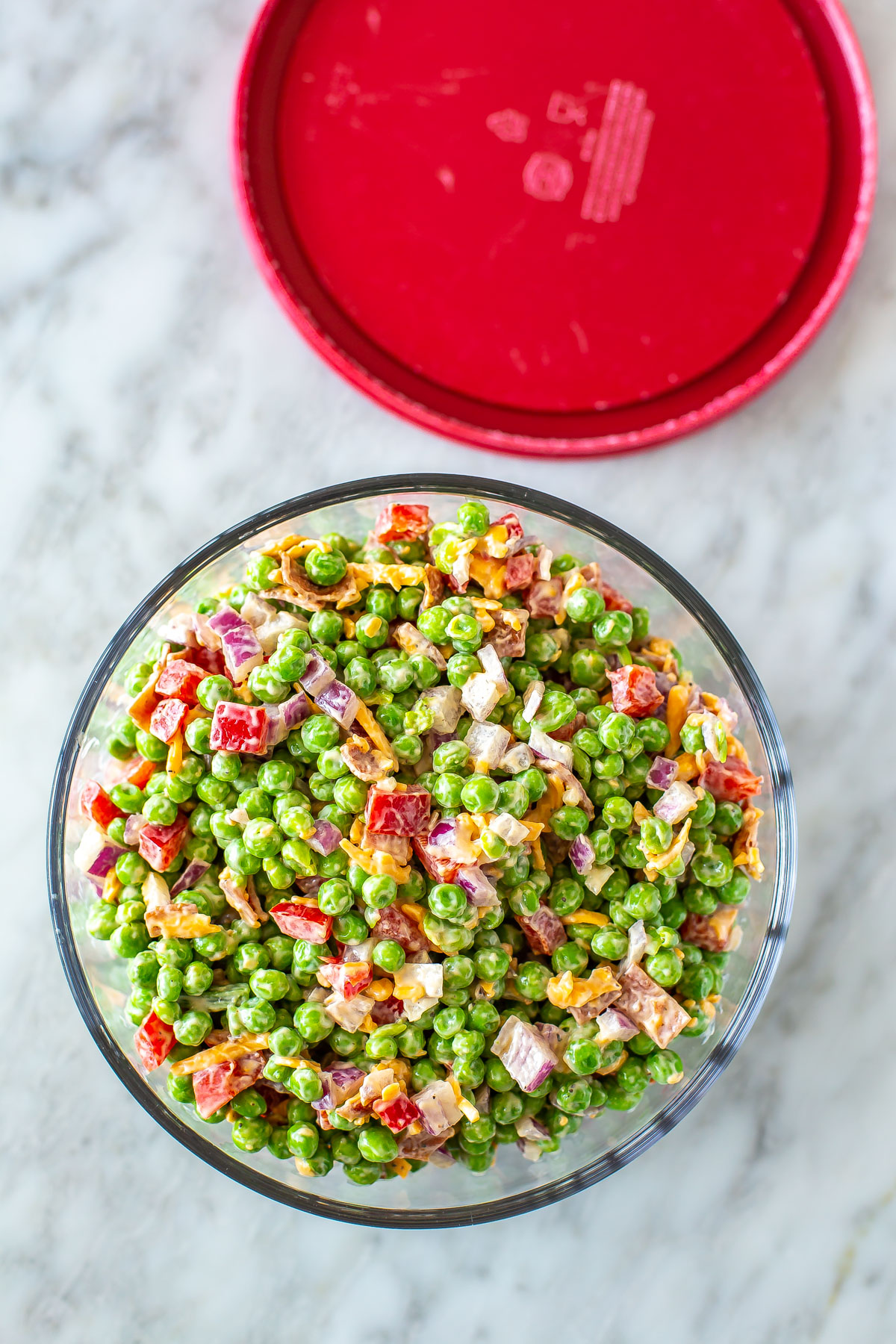 Creamy pea salad in a glass meal prep bowl with the lid off to the side.