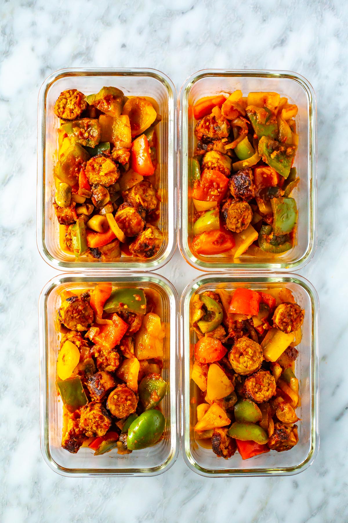 Four meal prep containers, each with a serving of sausage, peppers and onions.
