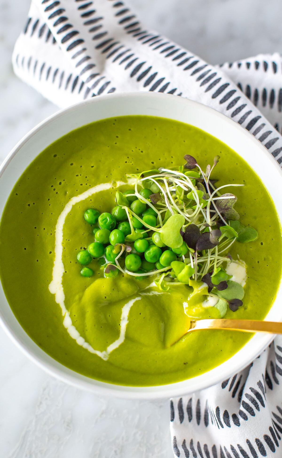 A close-up of a bowl of spring green pea soup with a spoon in it.