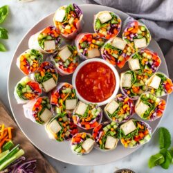 A large plate of summer rolls with a little bowl of sweet chili sauce in the middle.