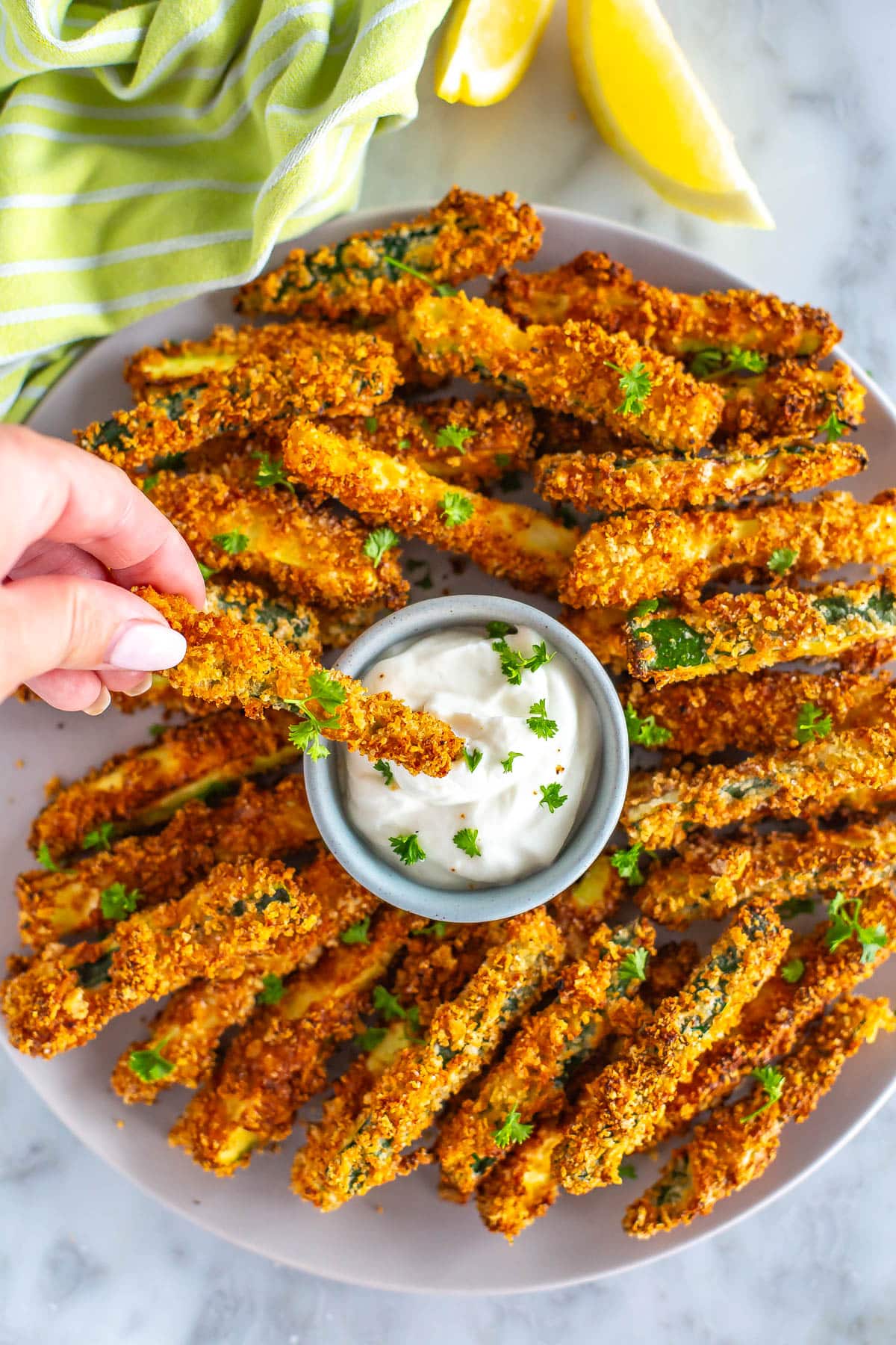 A plate of air fryer zucchini fries with one being dipped into garlic aioli.
