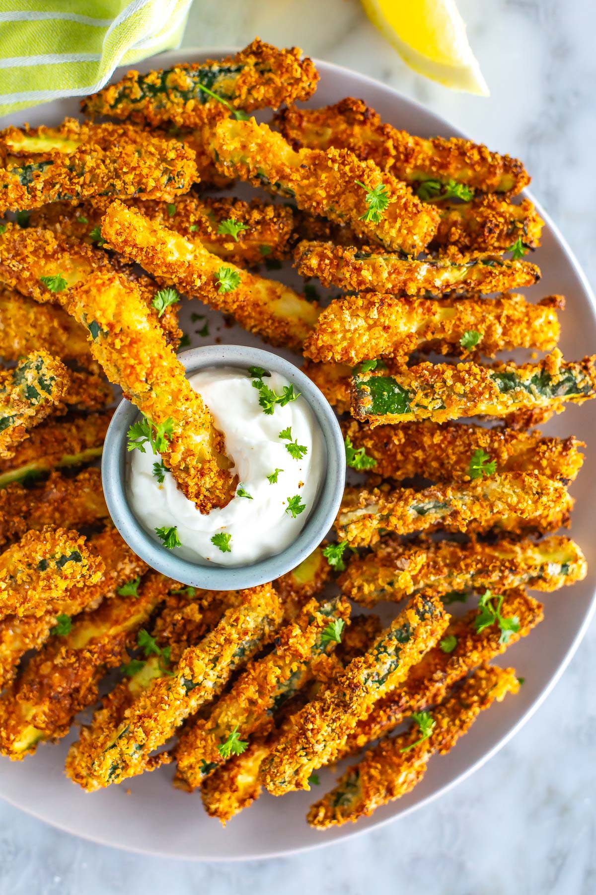 A close-up of a plate of air fryer zucchini fries, with one being dipped in garlic aioli.