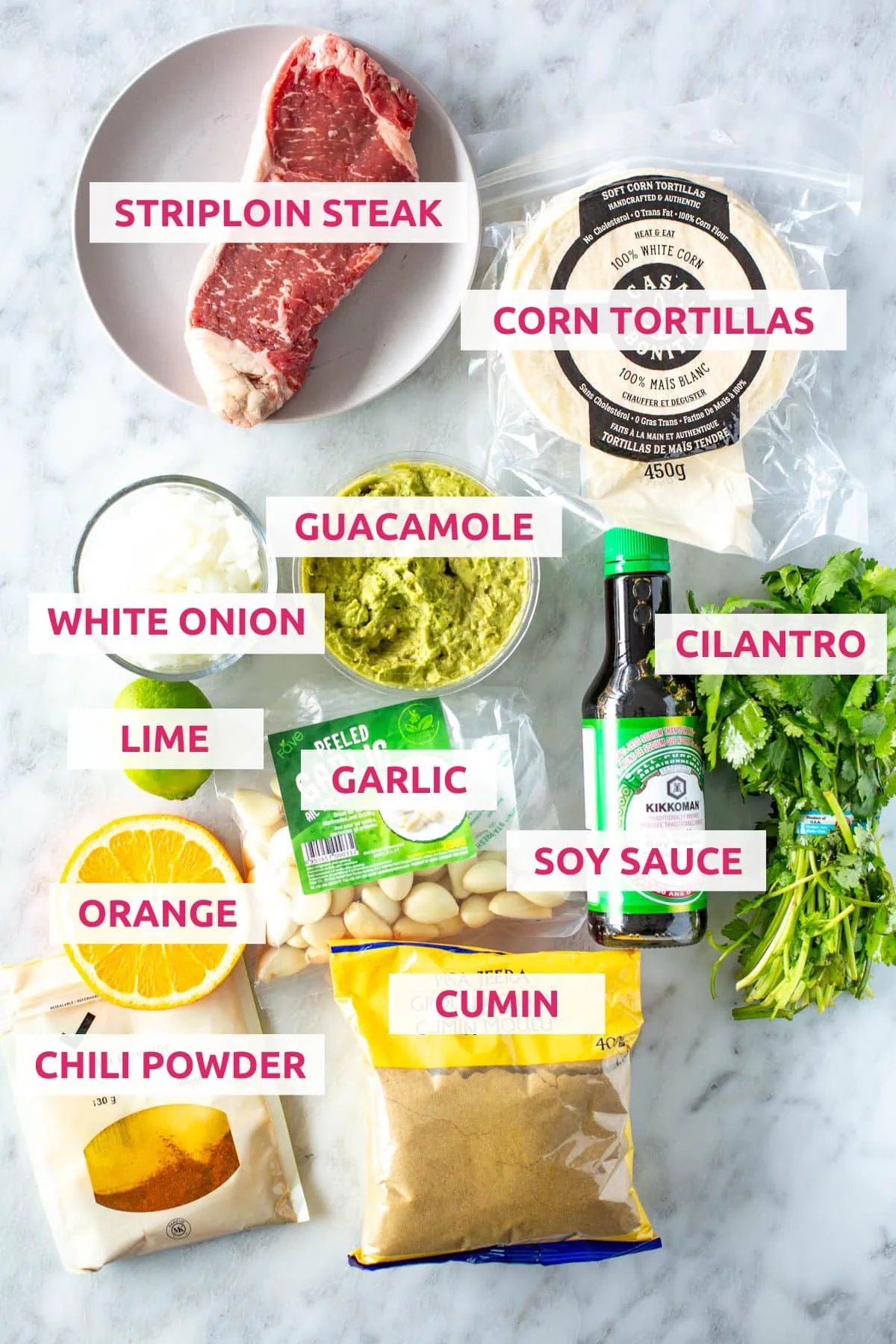 Ingredients for carne asada tacos: striploin steak, corn tortillas, white onion, guacamole, lime, garlic, soy sauce, cilantro, orange, chili powder and cumin