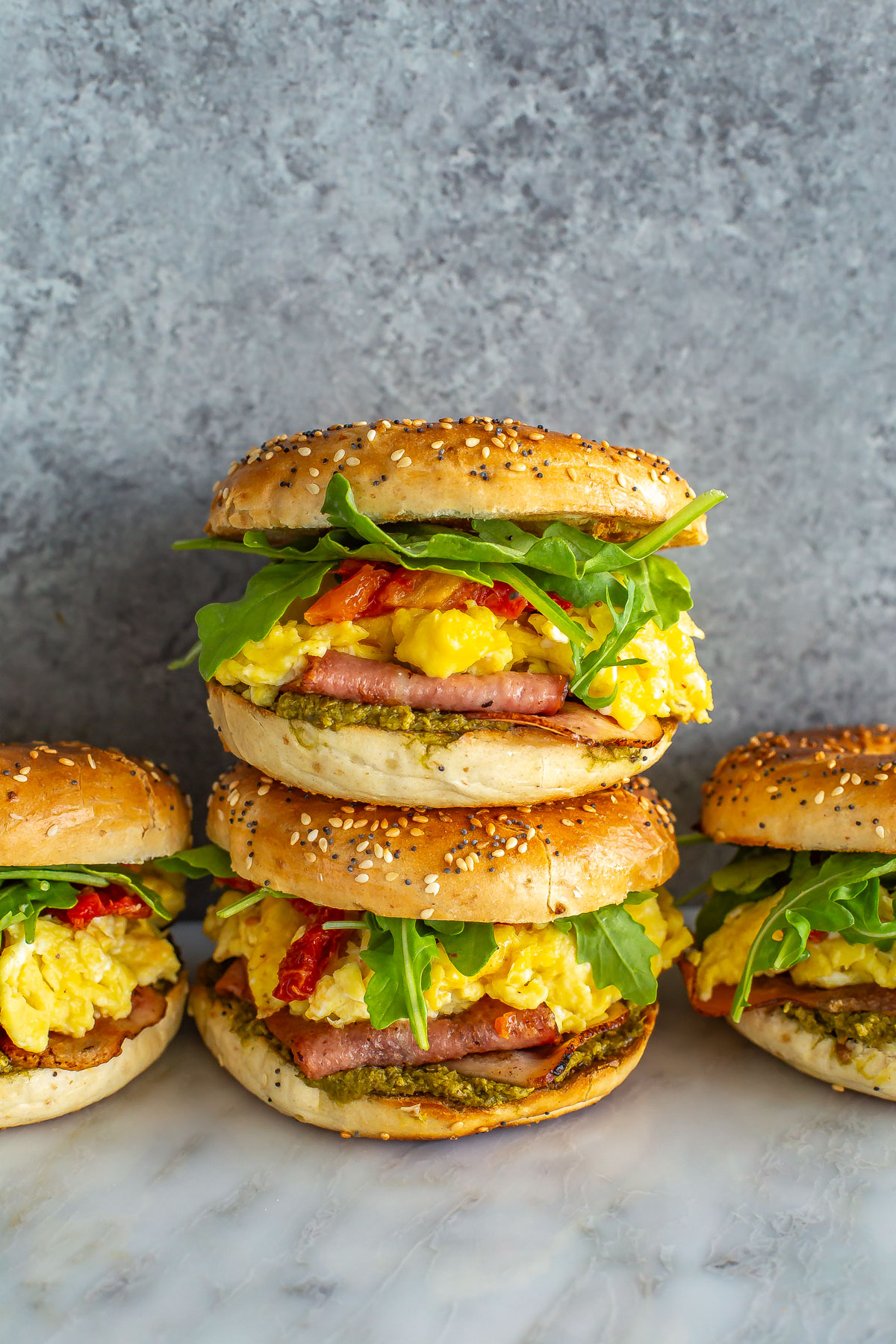 A close-up of a stack of pesto breakfast bagel sandwiches.