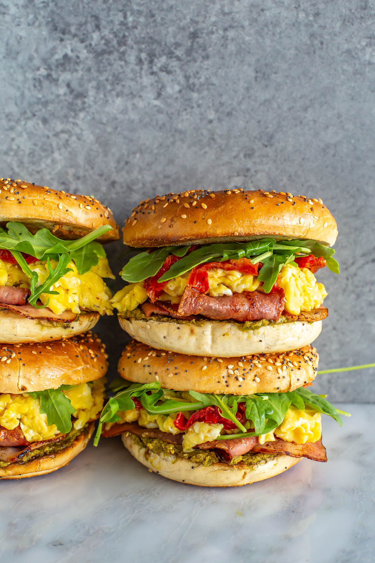Two stacks of two pesto breakfast bagel sandwiches.