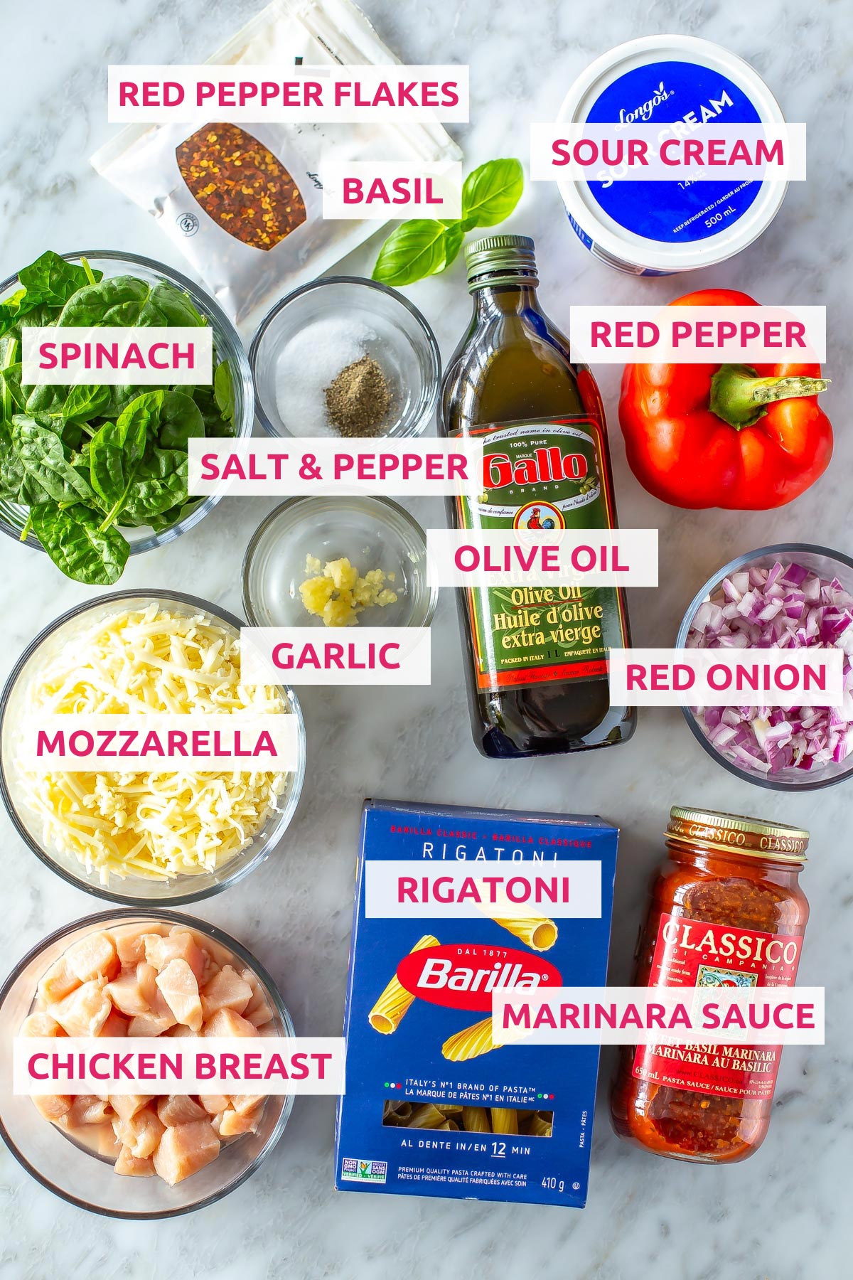 Ingredients for chicken pasta bake: chicken breasts, rigatoni, marinara sauce, mozzarella, garlic, olive oil, red onion, red pepper, spinach, salt, pepper, sour cream, basil and red chili flakes.