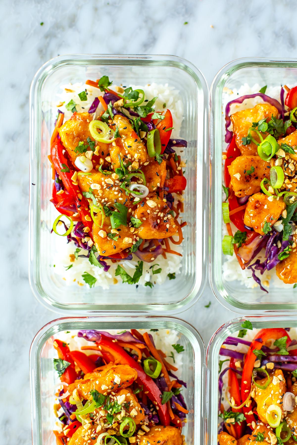 Four meal prep containers with sweet chili chicken inside.