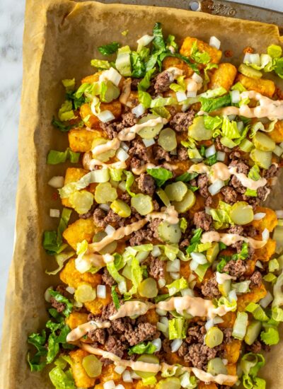 A close-up of big mac tater tot nachos on a baking sheet covered with parchment paper.